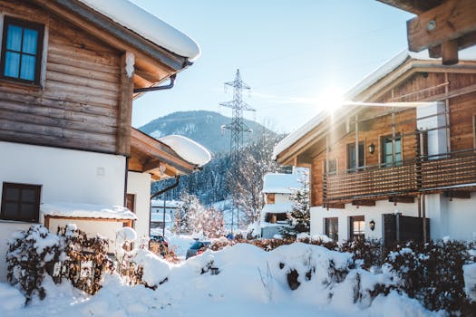 Snow-covered wooden chalets and mountains in Liezen, Austria under bright sunlight.